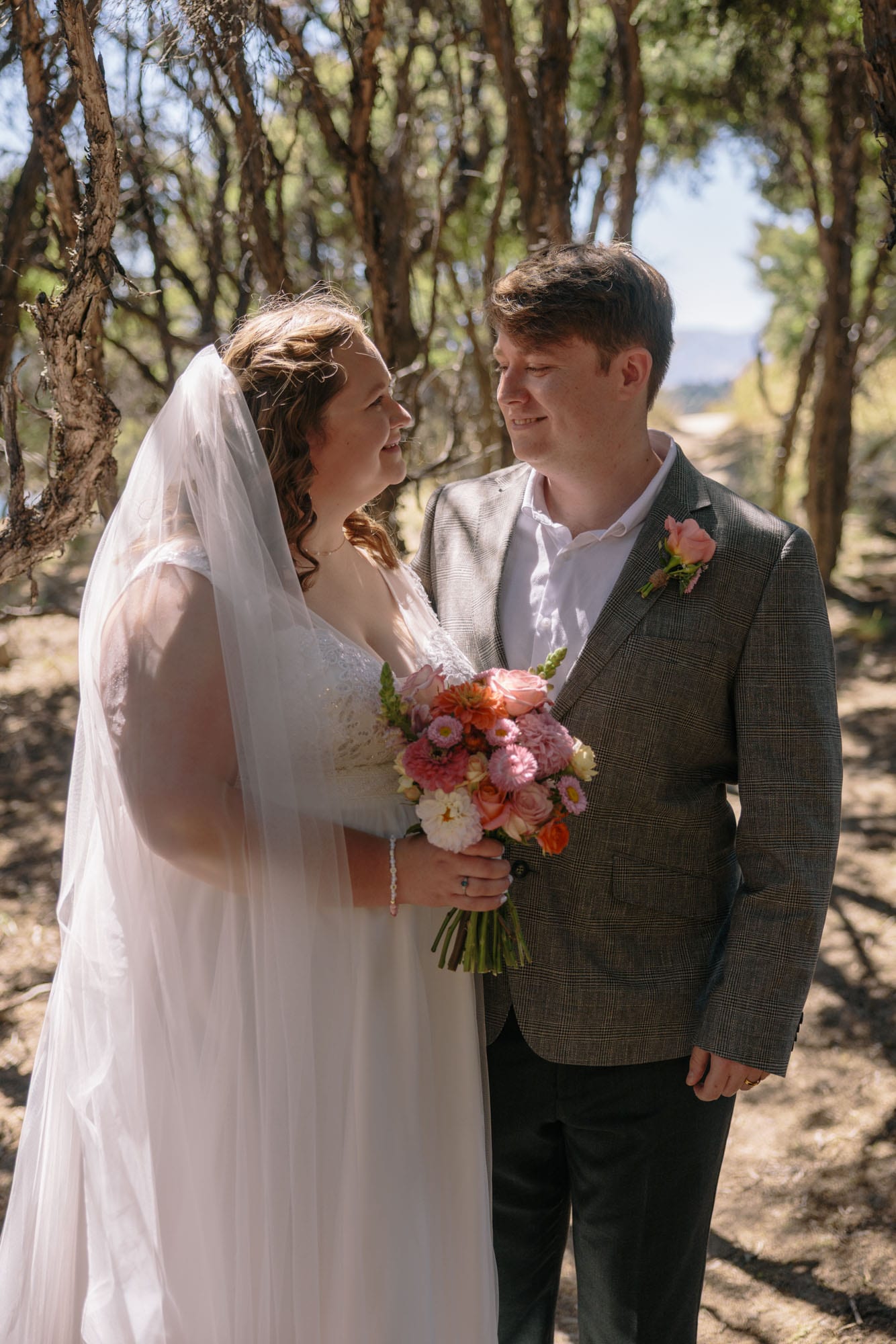 A bride holding a bright bouquet beside her groom in tweed